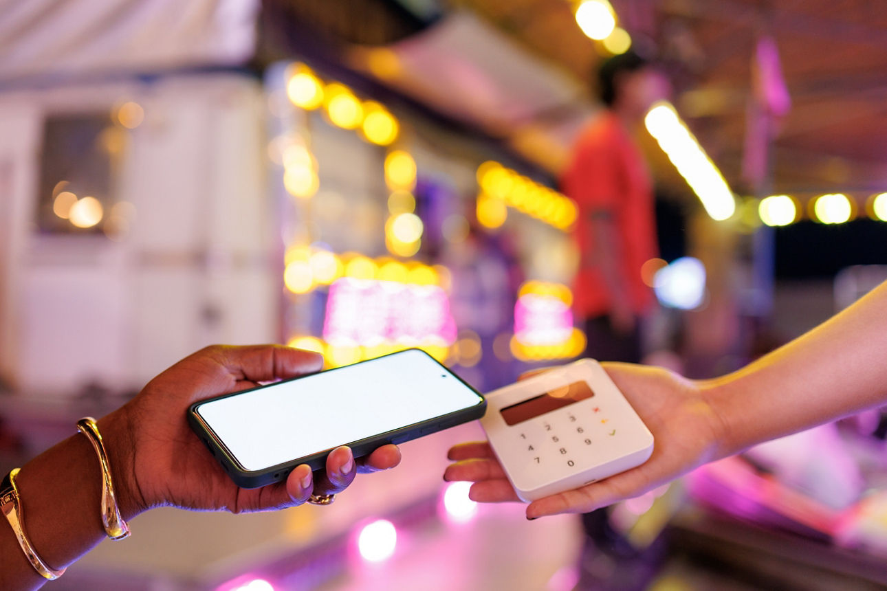 Jemand bezahlt mit einem Handy an einem Bezahlgerät, welches in einer anderen Hand gehalten wird.