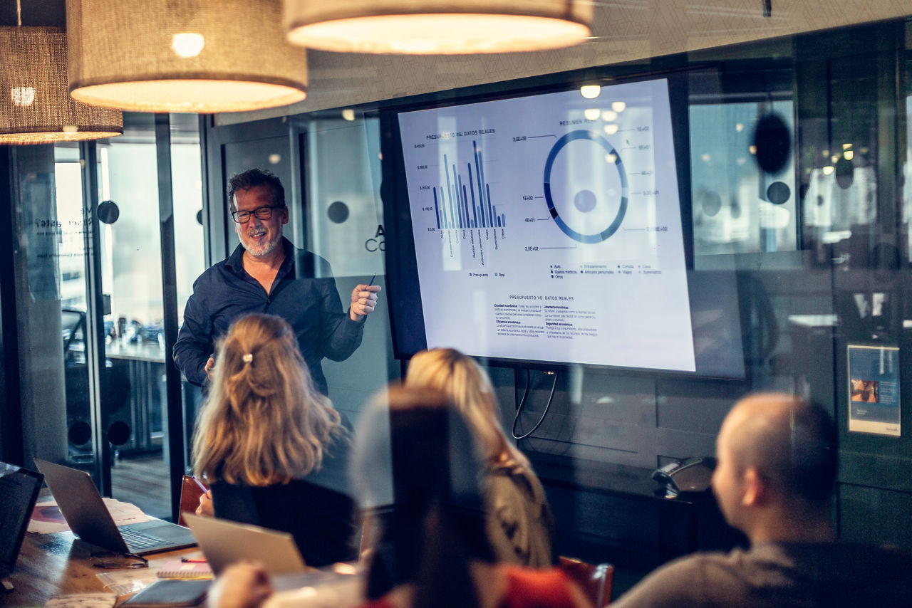Foto eines erwachsenen Mannes, der eine Finanzpräsentation über Grafiken und Analysen in einem modernen Konferenzraum in einem Bürogebäude hält