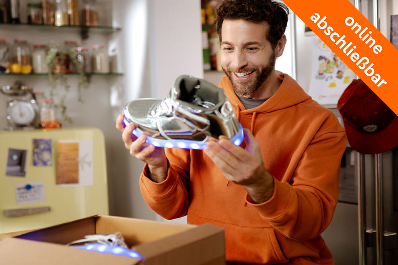 Junger Mann sitzt in der Küche und packt einen Sneaker aus