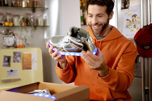 Junger Mann sitzt in der Küche und packt einen Sneaker aus