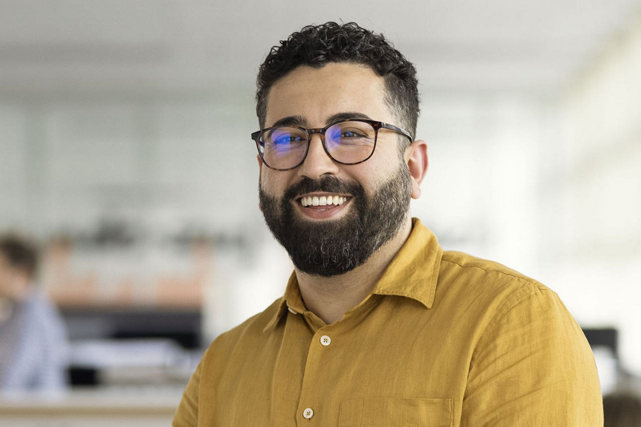 Ein junger Mann mit Brille und Bart lächelt freundlich in die Kamera
