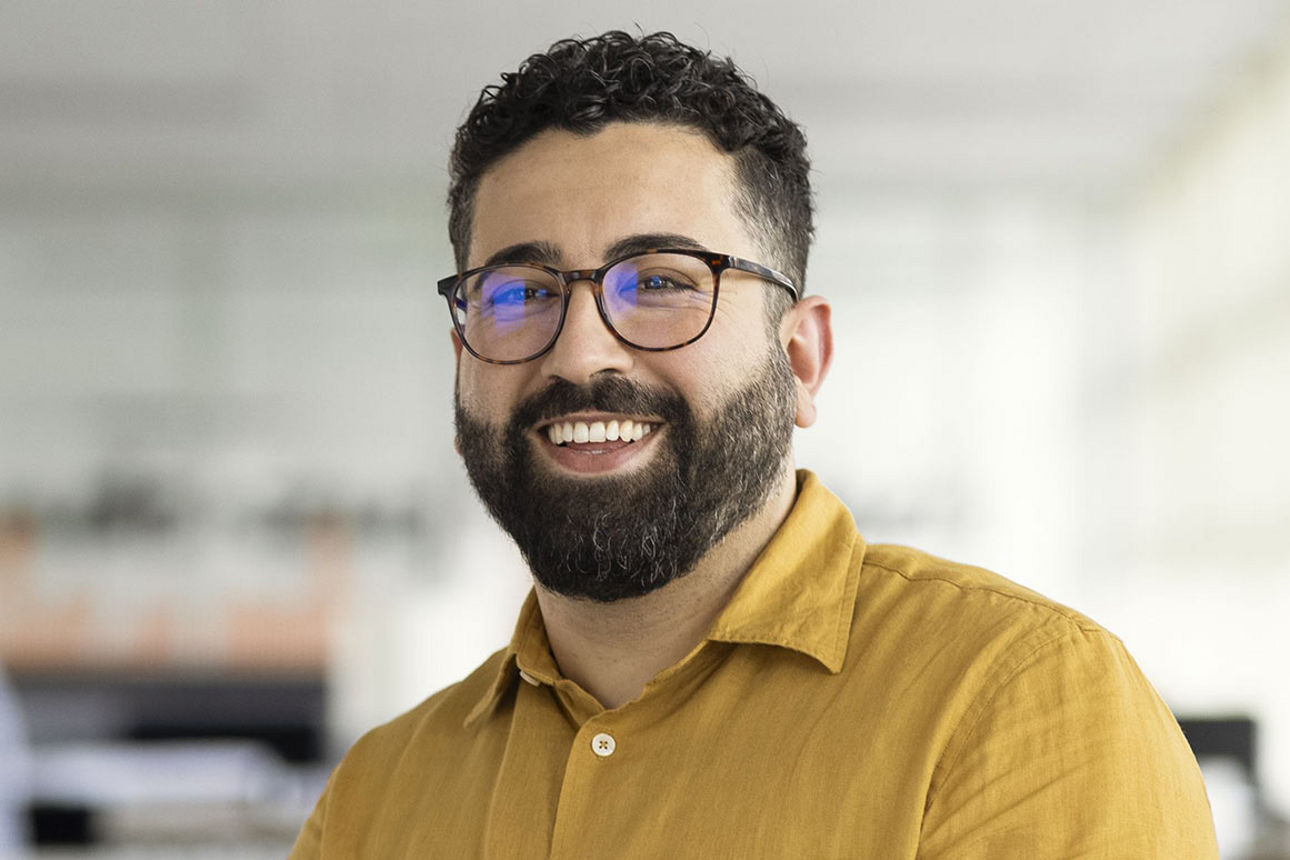Ein junger Mann mit Brille und Bart lächelt freundlich in die Kamera