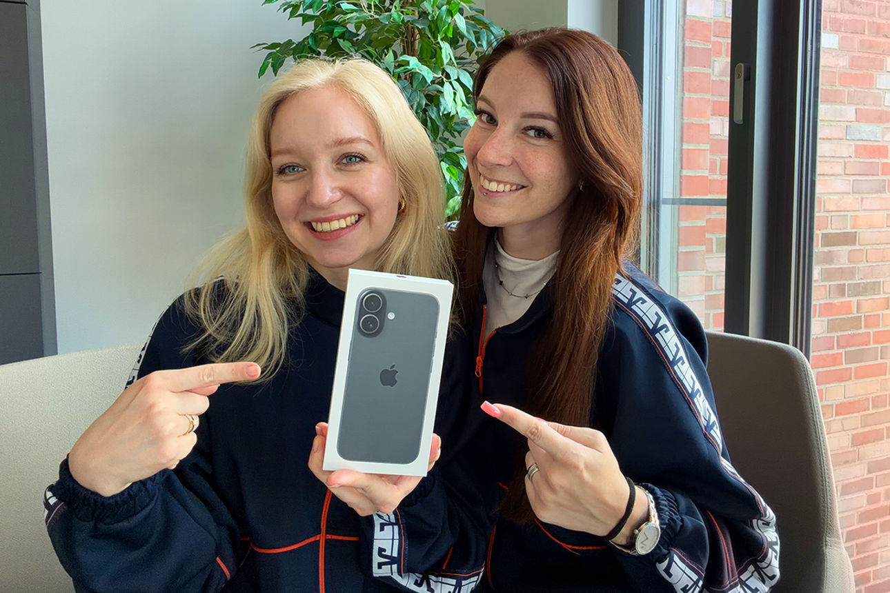 Zwei junge Frauen zeigen lächelnd auf ein iPhone 17.
