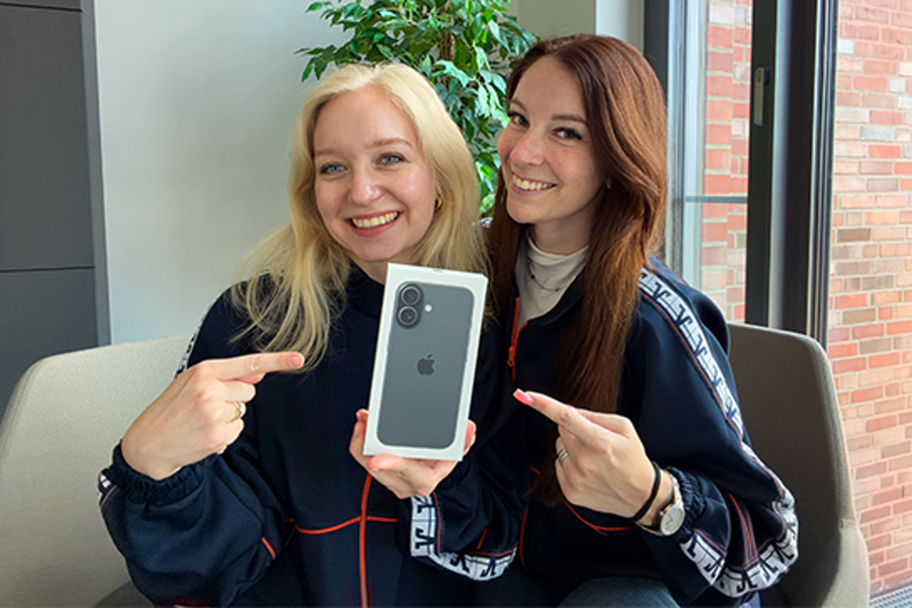 Zwei junge Frauen zeigen lächelnd auf ein iPhone 17.