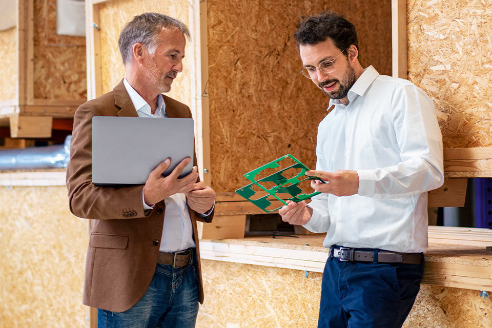 Zwei Männer sprechen in einer Werkstatt über Schablonen, die einer der beiden in der Hand hält