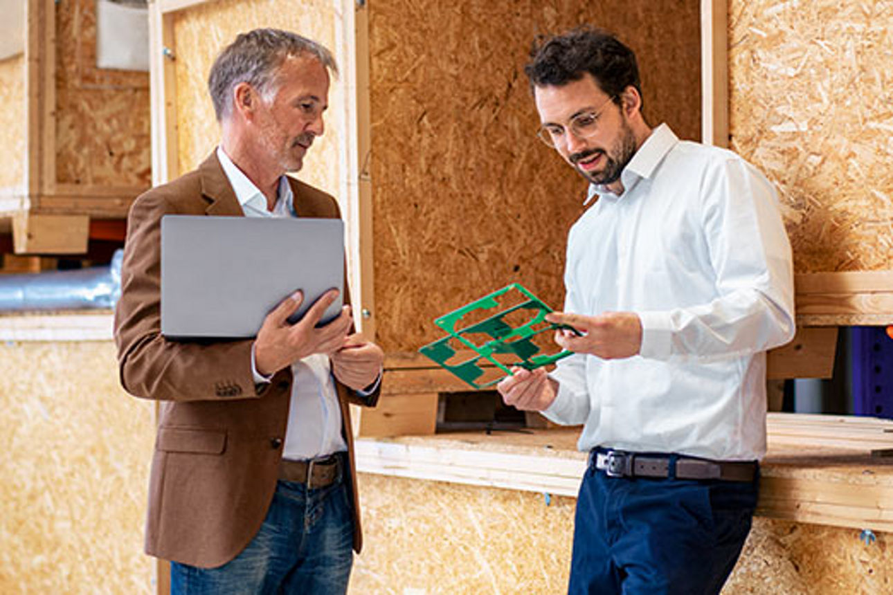 Zwei Männer sprechen in einer Werkstatt über Schablonen, die einer der beiden in der Hand hält