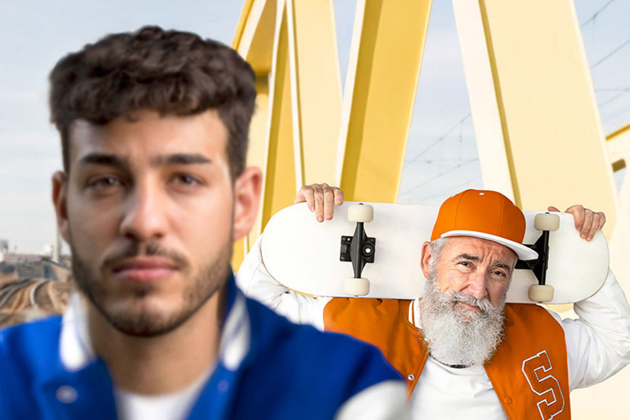 Junger Mann steht im Vordergrund, älterer Mann mit Skateboard im Hintergrund