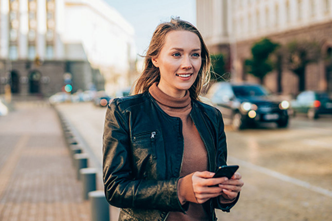 Junge Dame mit Handy in der Hand läuft am Straßenrand