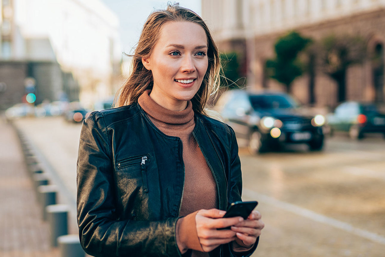 Eine Frau hat ein Handy in der Hand und läuft über eine Straße.