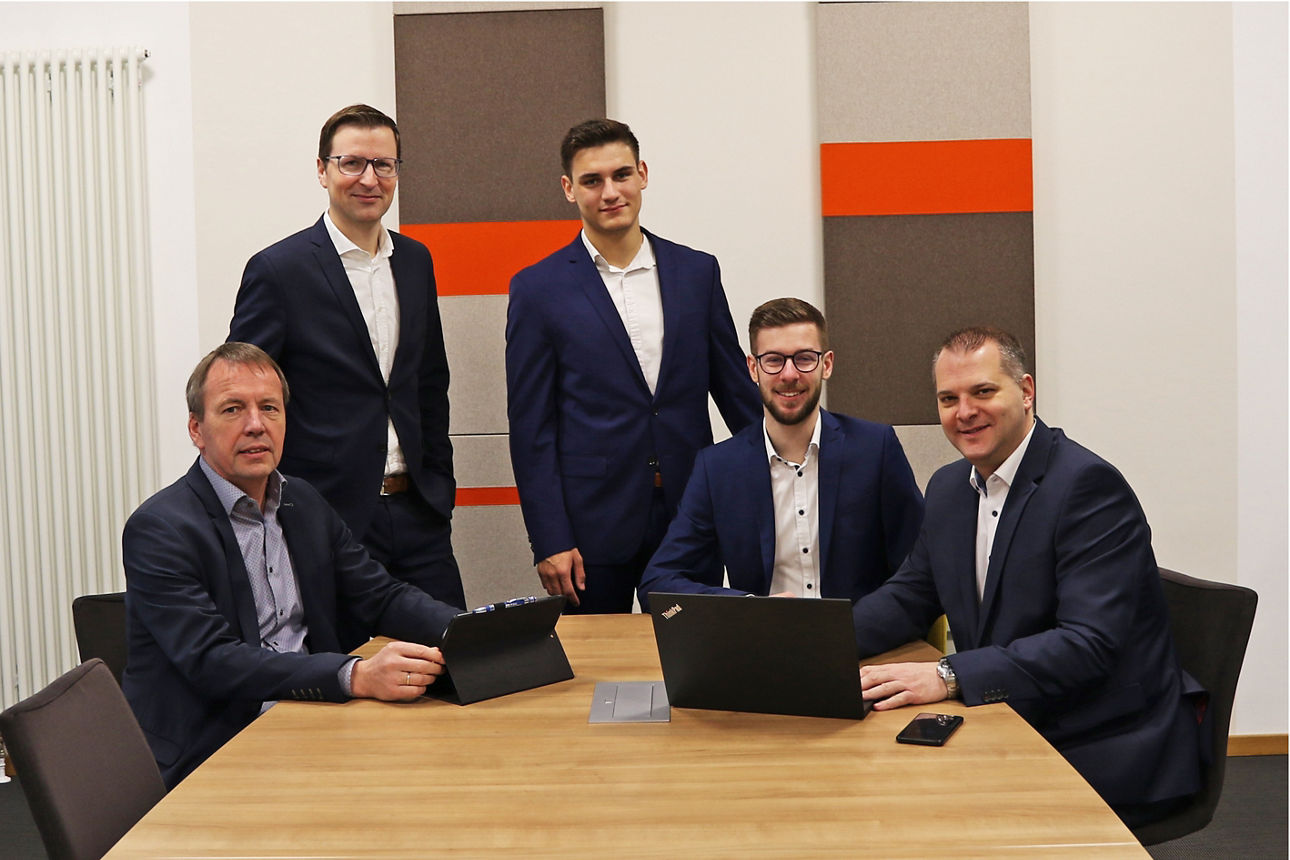 eBusiness-Berater Teamfoto mit fünf Männern im Konferenzraum vor farbigen Wandpaneelen.