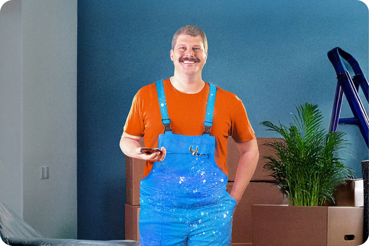 Mann steht in seiner Wohnung mit Latzhose