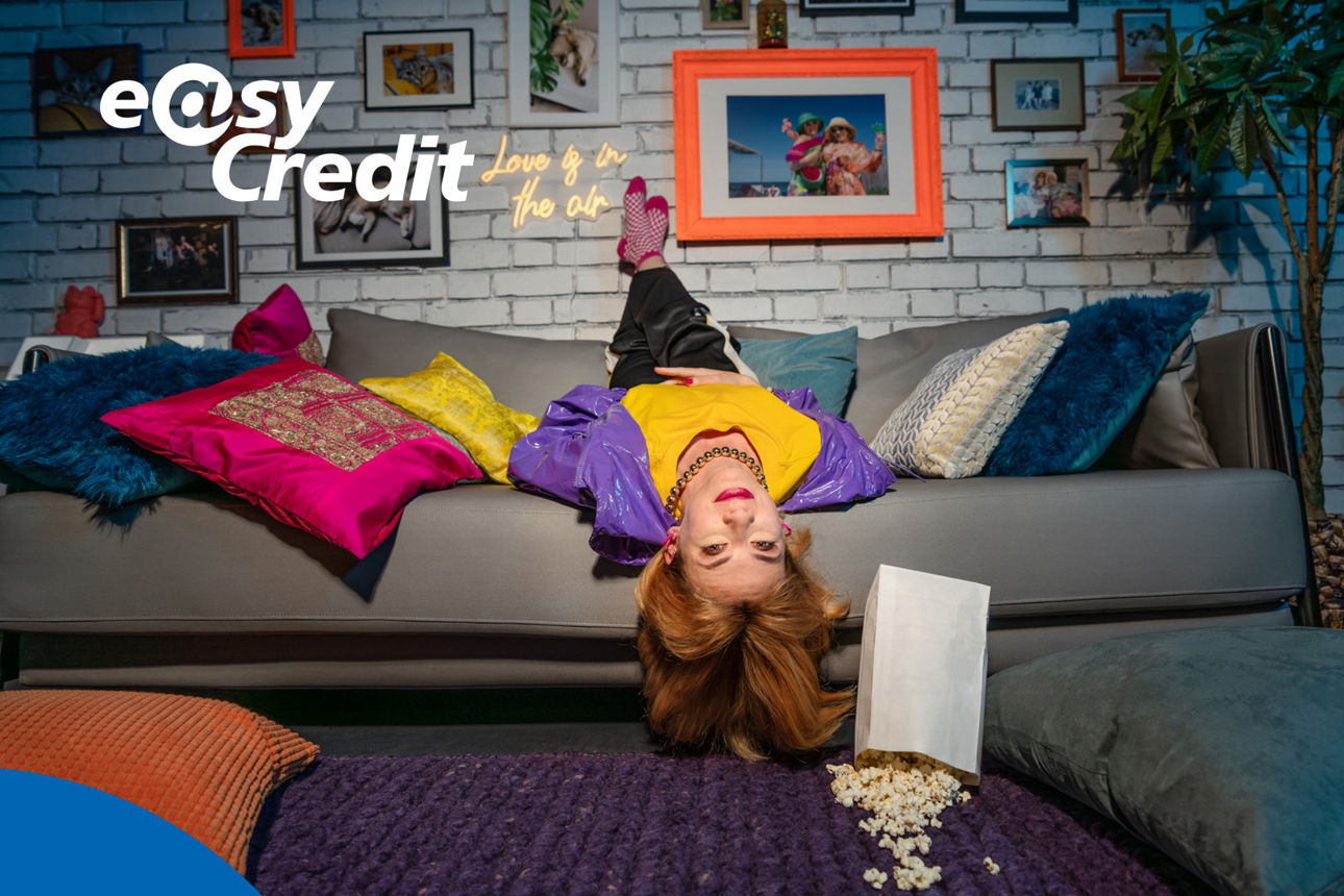 Junge Frau liegt falsch rum auf dem Sofa, neben ihr eine Tüte Popcorn.