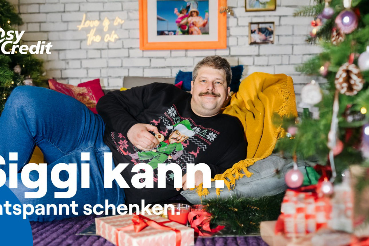 Ein Mann im Weihnachtspullover liegt entspannt auf seinem Sofa