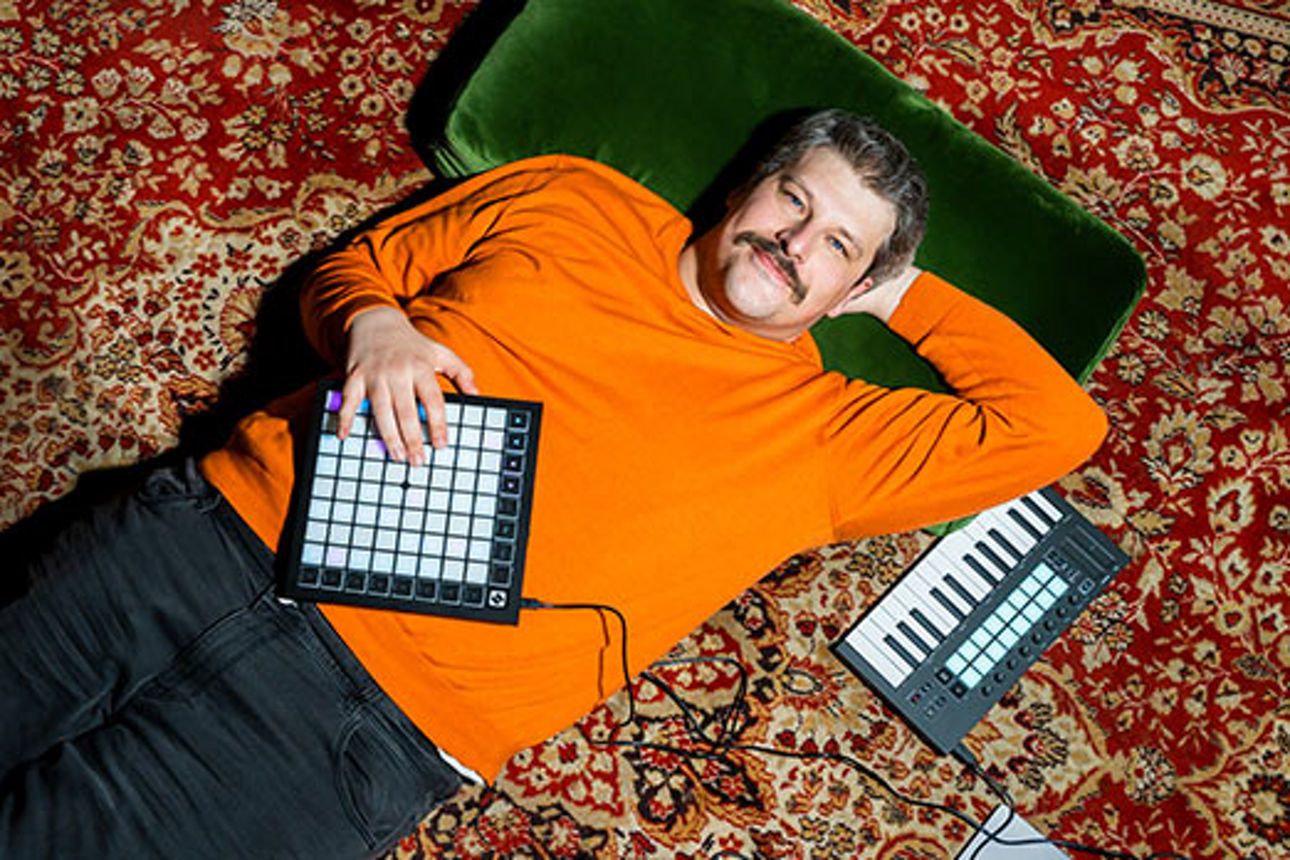 Mann liegt umgeben von Keyboards und Laptop entspannt auf einem Teppich