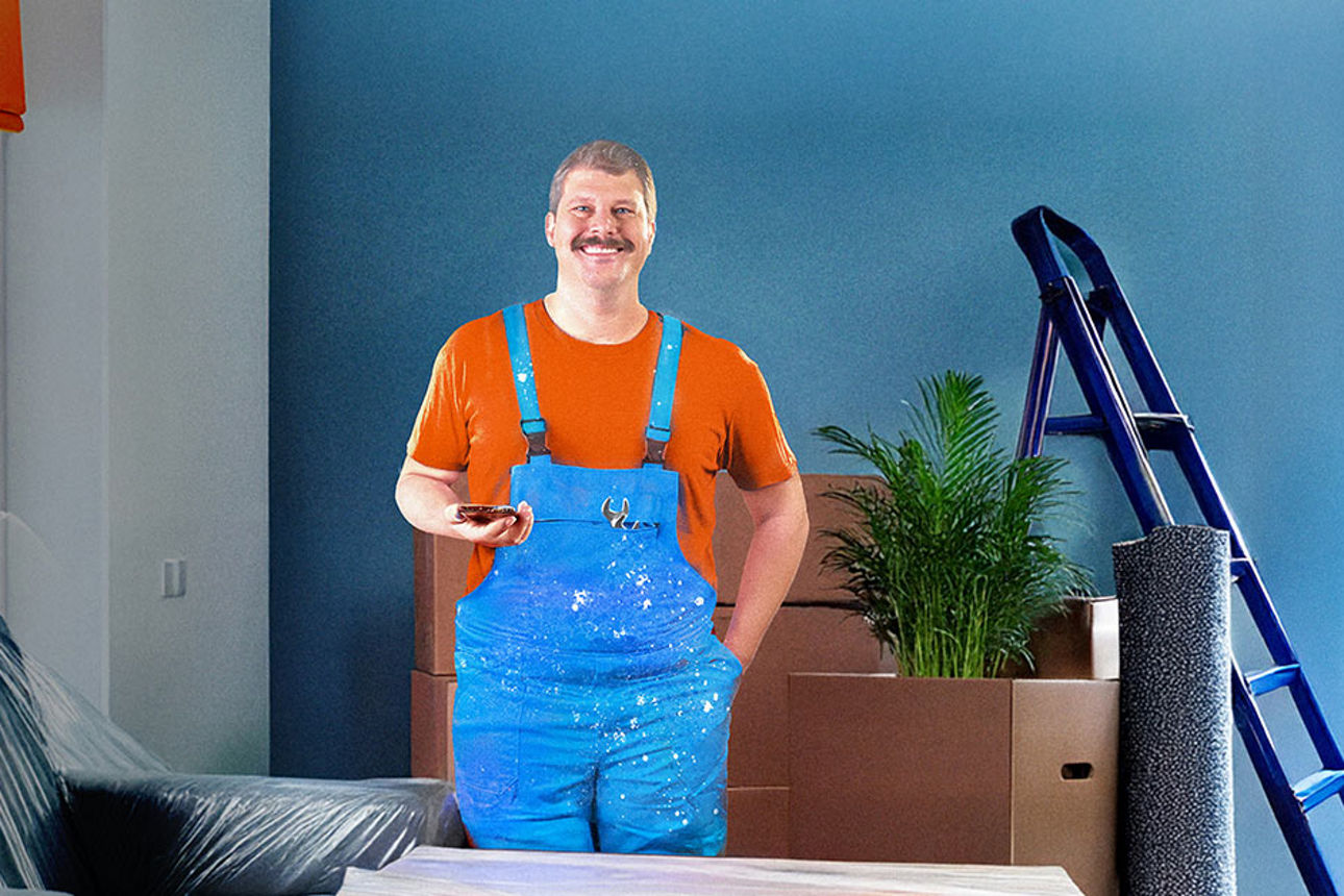 Mann in Arbeitskleidung steht lächelnd in einem frisch renovierten Raum.