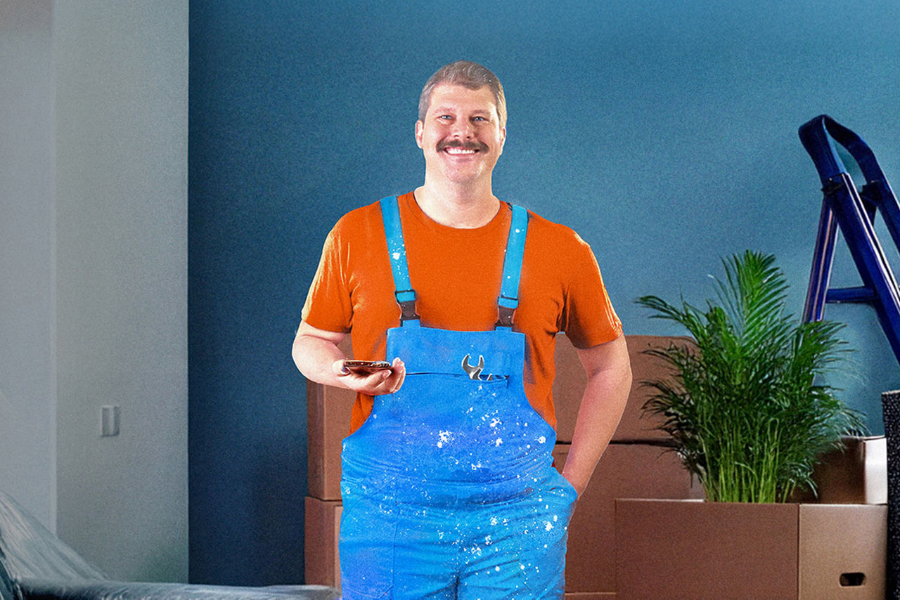 Mann steht in seiner Wohnung mit Latzhose