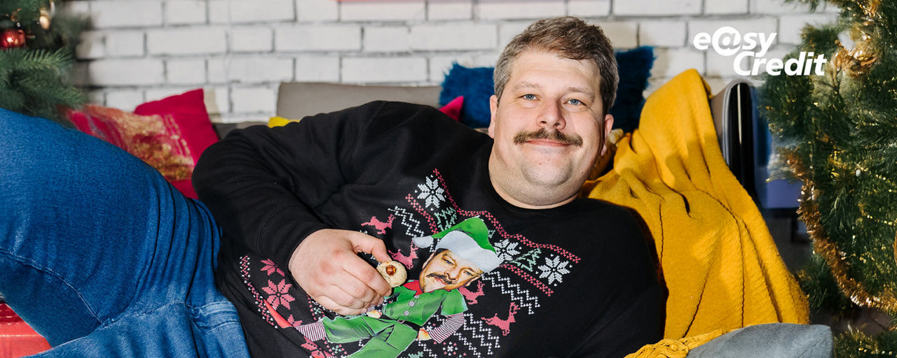Mann im Weihnachtspullover liegt bequem auf der Couch