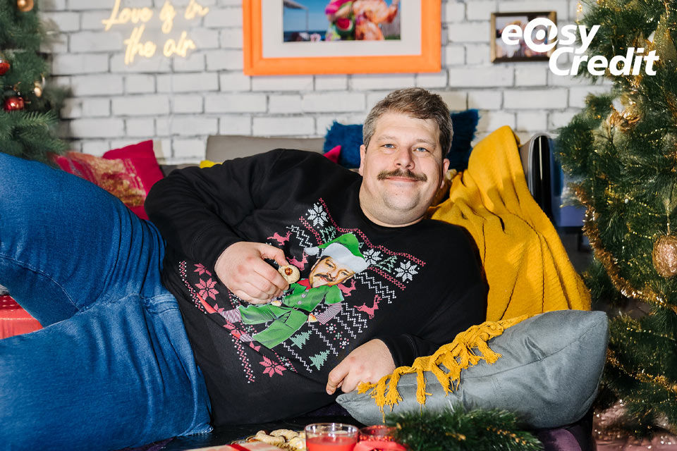 Mann im Weihnachtspullover liegt bequem auf der Couch