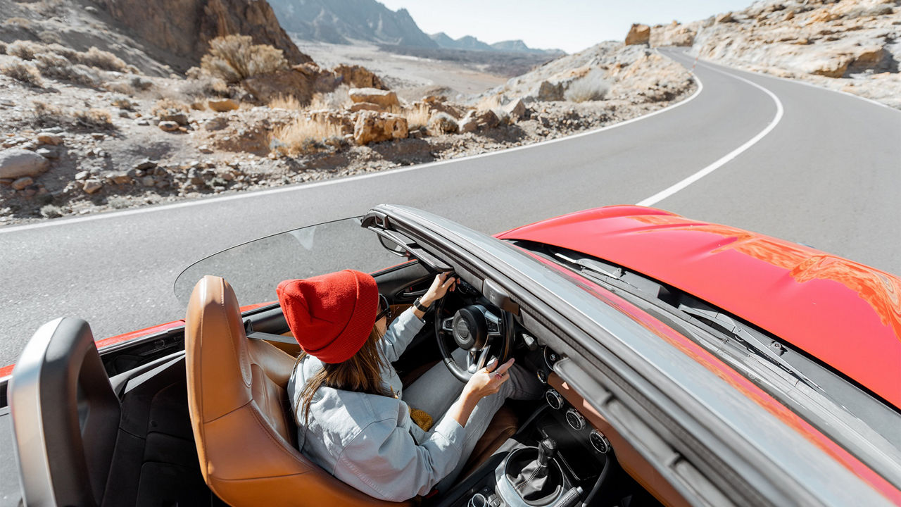 Junge Frau fährt mit einem roten Cabrio durch eine karge Landschaft