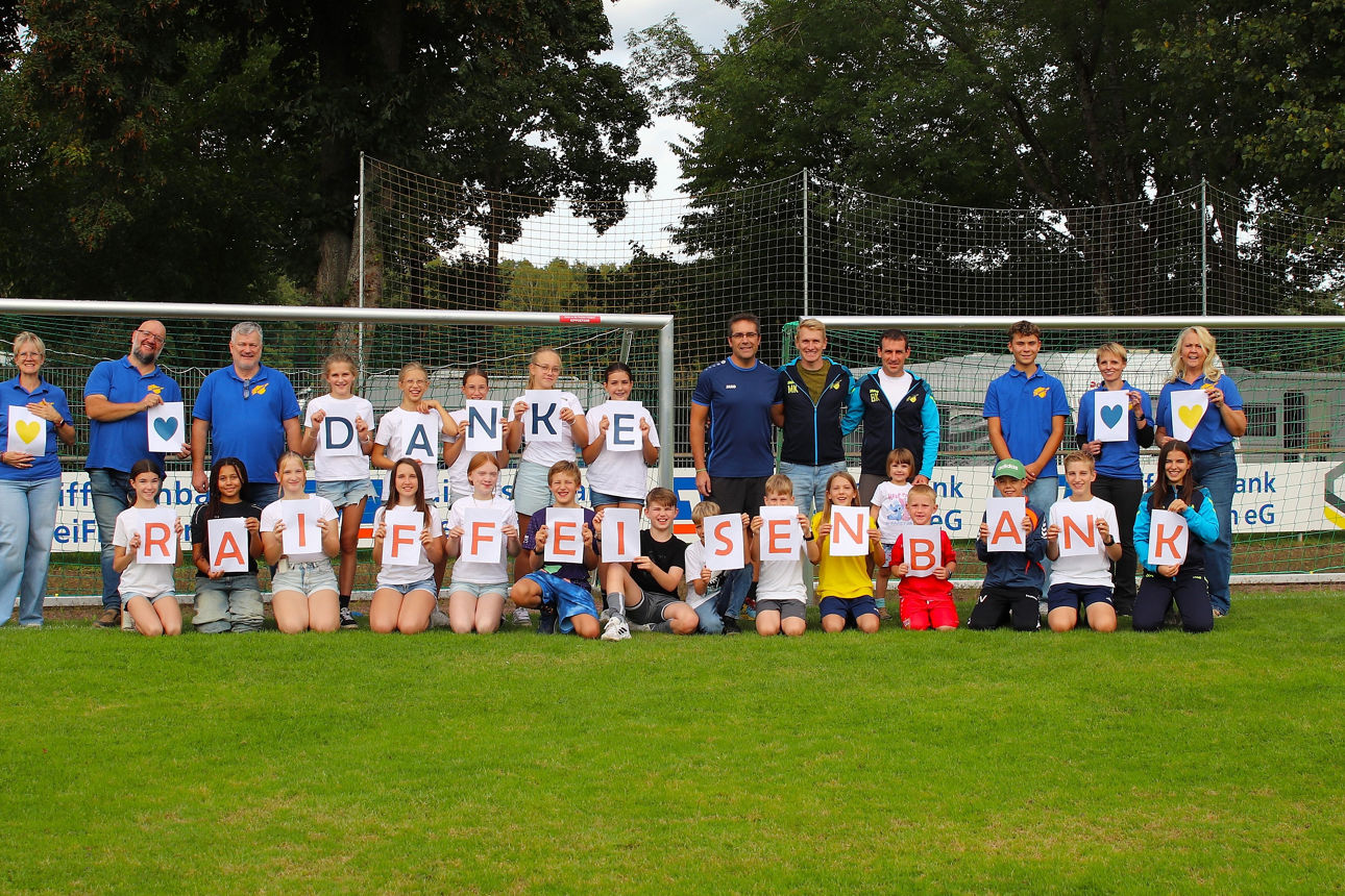 Vereinsmitglieder halten den Schriftzug "Danke Raiffeisenbank" auf einem Fußballplatz in die Höhe