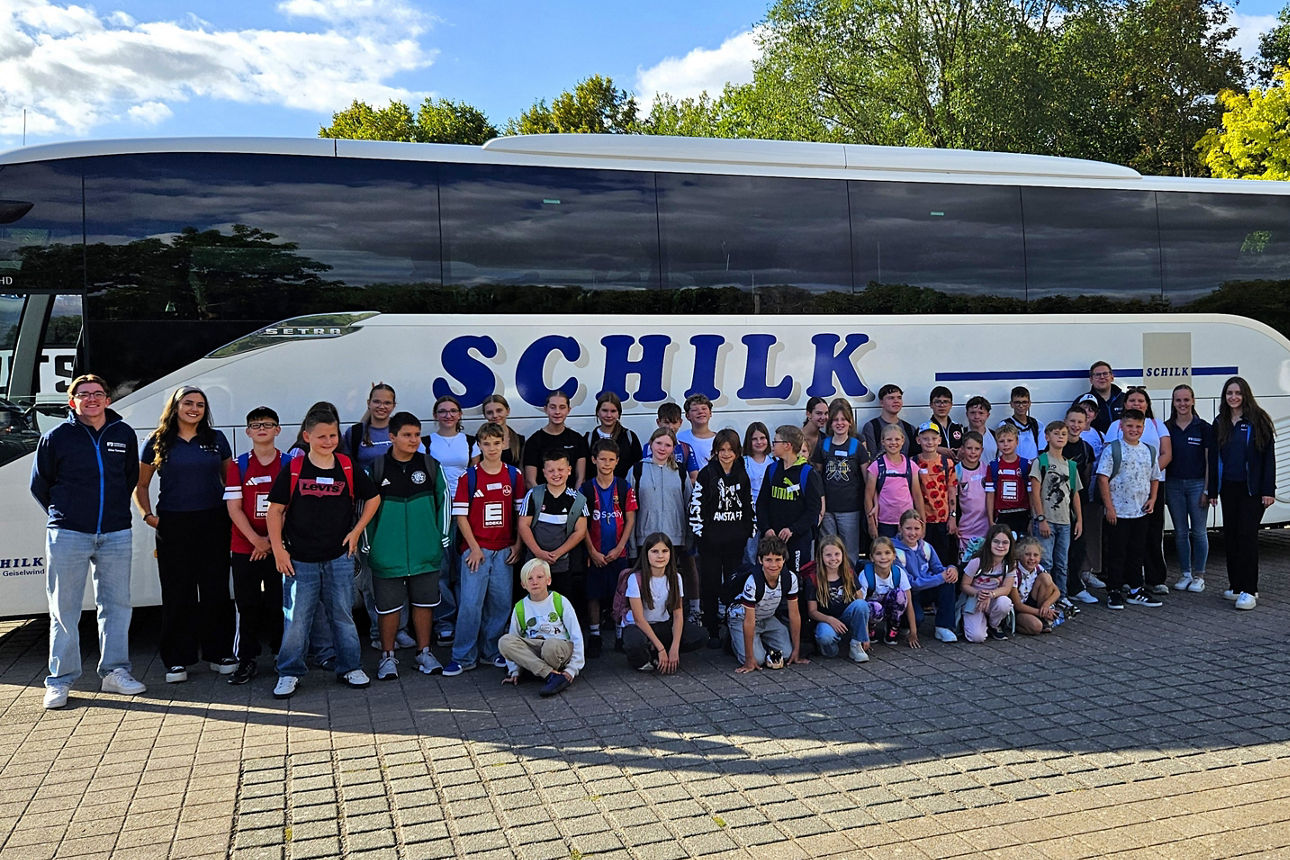 Das Team des Jugendmarkts steht mit einer Gruppe von Kindern vor einem Reisebus