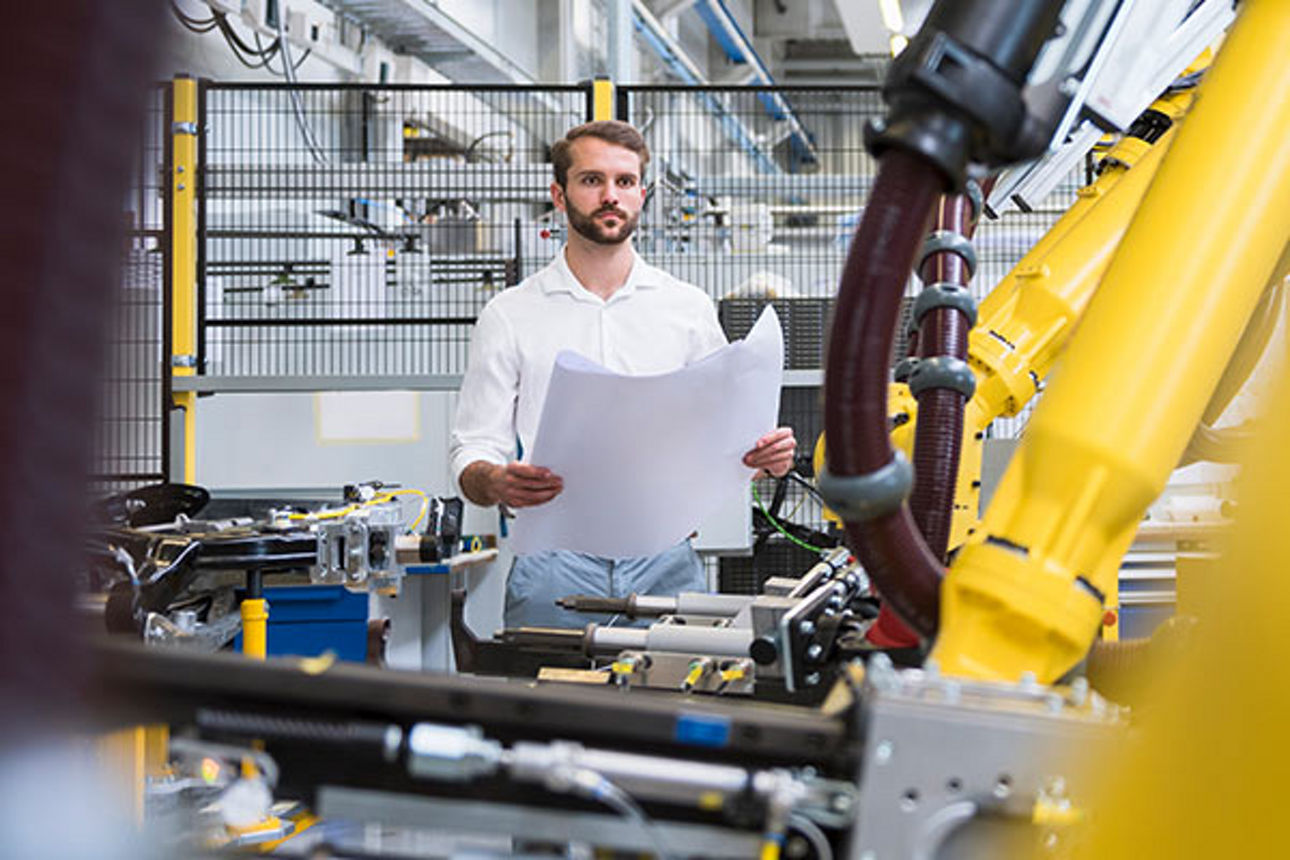 Mann schaut über Planskizze auf Roboterarm