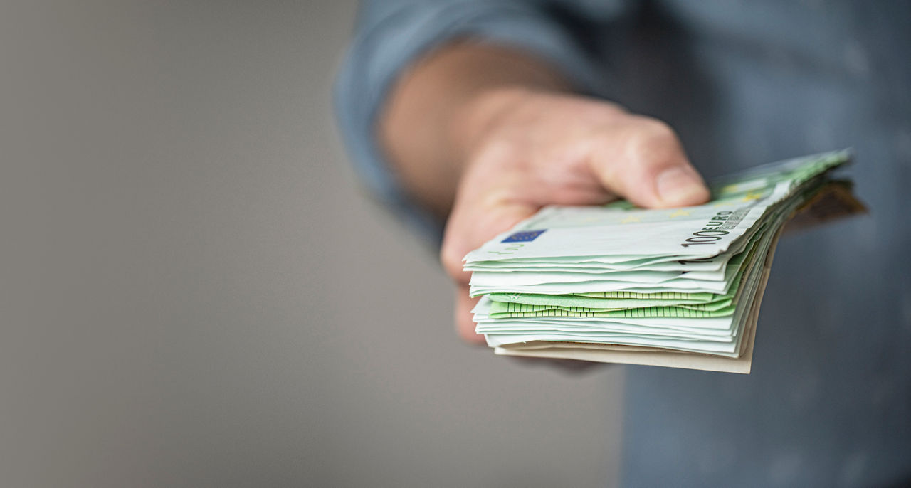 Eine Hand überreicht ein Bündel Geldscheine