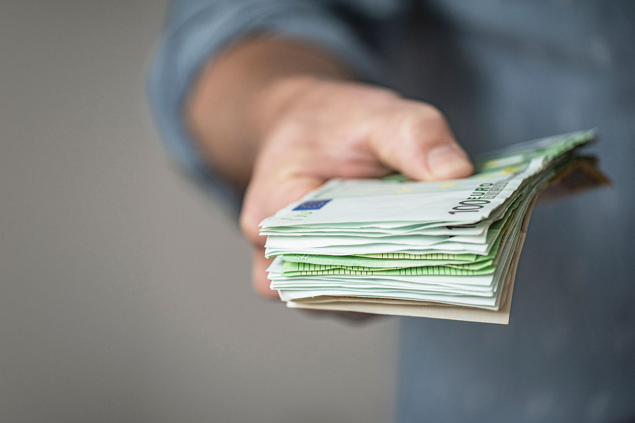 Eine Hand überreicht ein Bündel Geldscheine