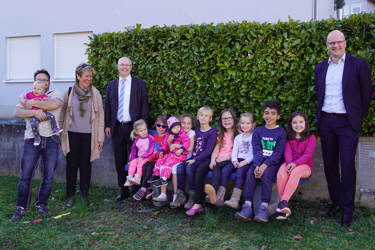 Eine gruppe von Erwachsenen und Kindern, sitzen und stehen vor einer Hecke