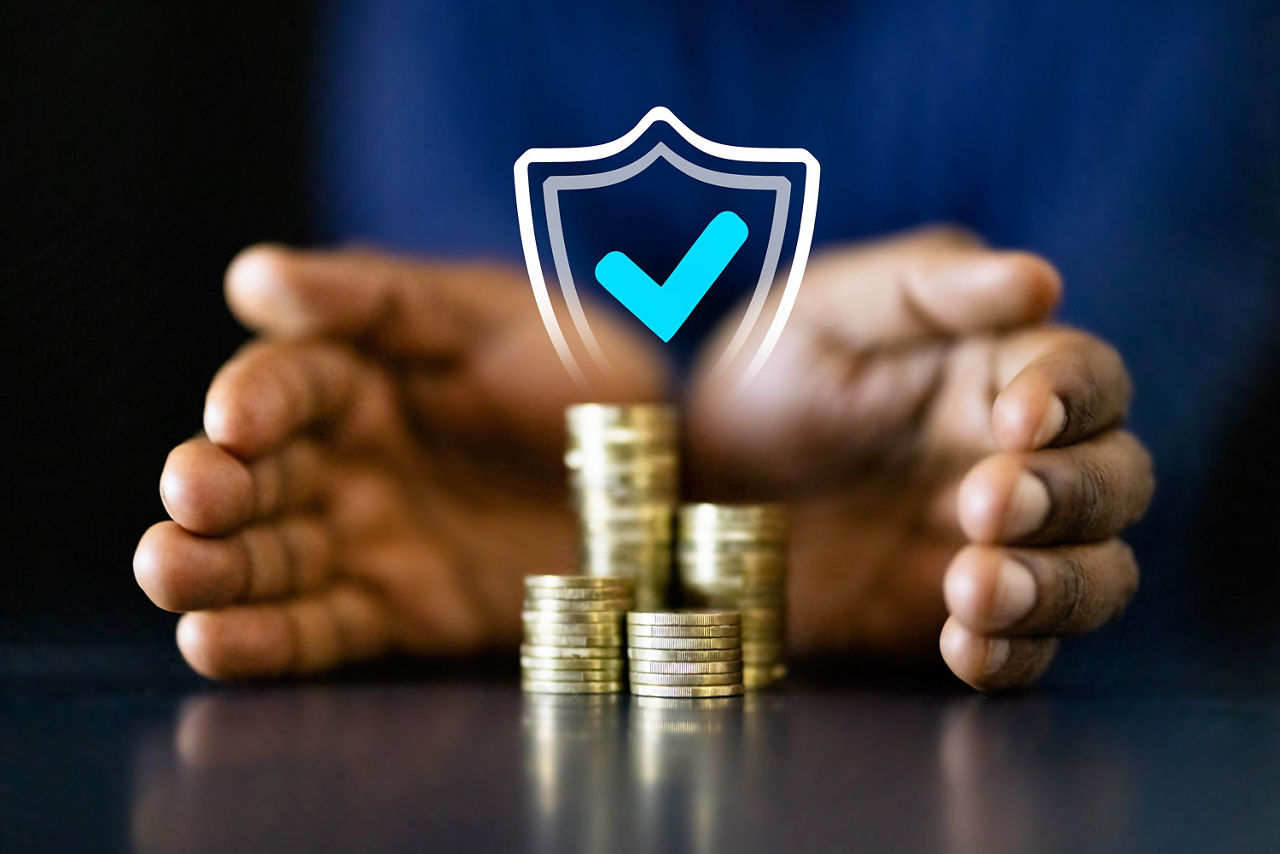 Zwei Hände umschließen einen Stapel Münzen. Darüber ist ein Schild mit einem blauen Hacken projiziert, dass die Sicherheit des Geldes symbolisiert.