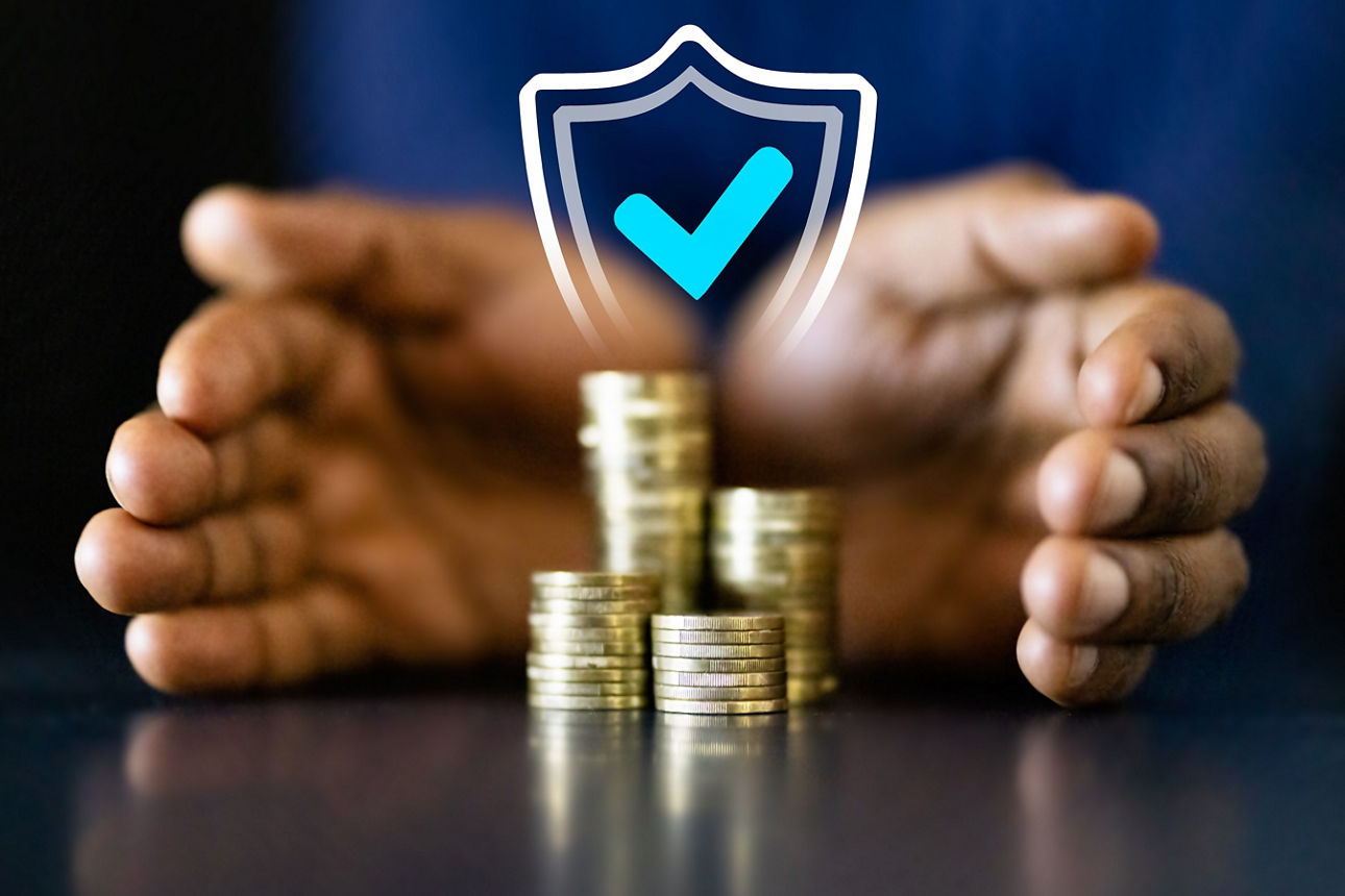 Zwei Hände umschließen einen Stapel Münzen. Darüber ist ein Schild mit einem blauen Hacken projiziert, dass die Sicherheit des Geldes symbolisiert.