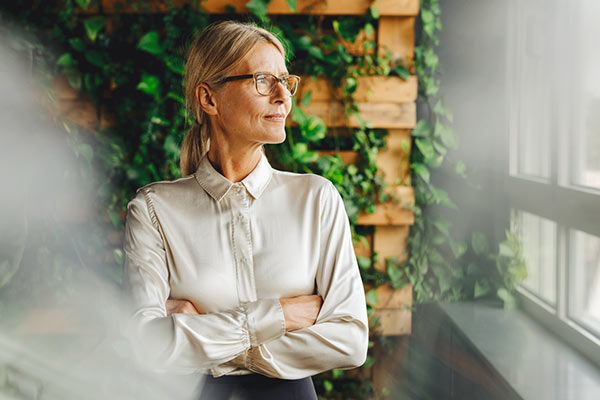 Eine Geschäftsfrau schaut mit verschränkten Armen aus dem Fenster