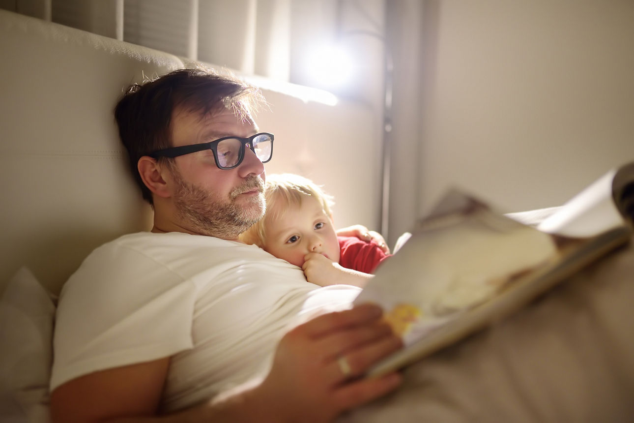 Ein Vater liest seinem Kind eine Gute-Nacht-Geschichte vor und legt seinen Sohn danach schlafen. Gemeinsame Zeit in der Familie.