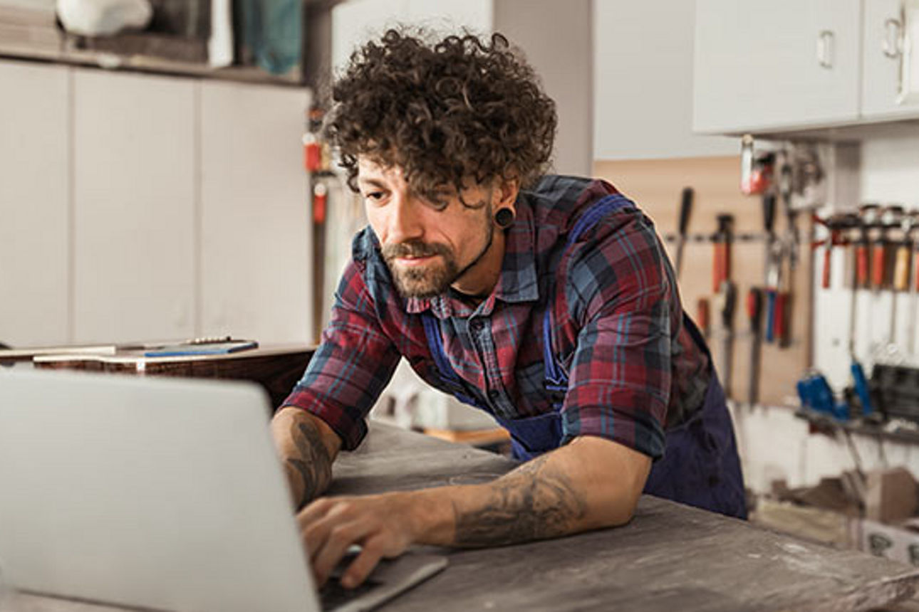 Junger Mann mit locken und Laptop in einer Werkstatt