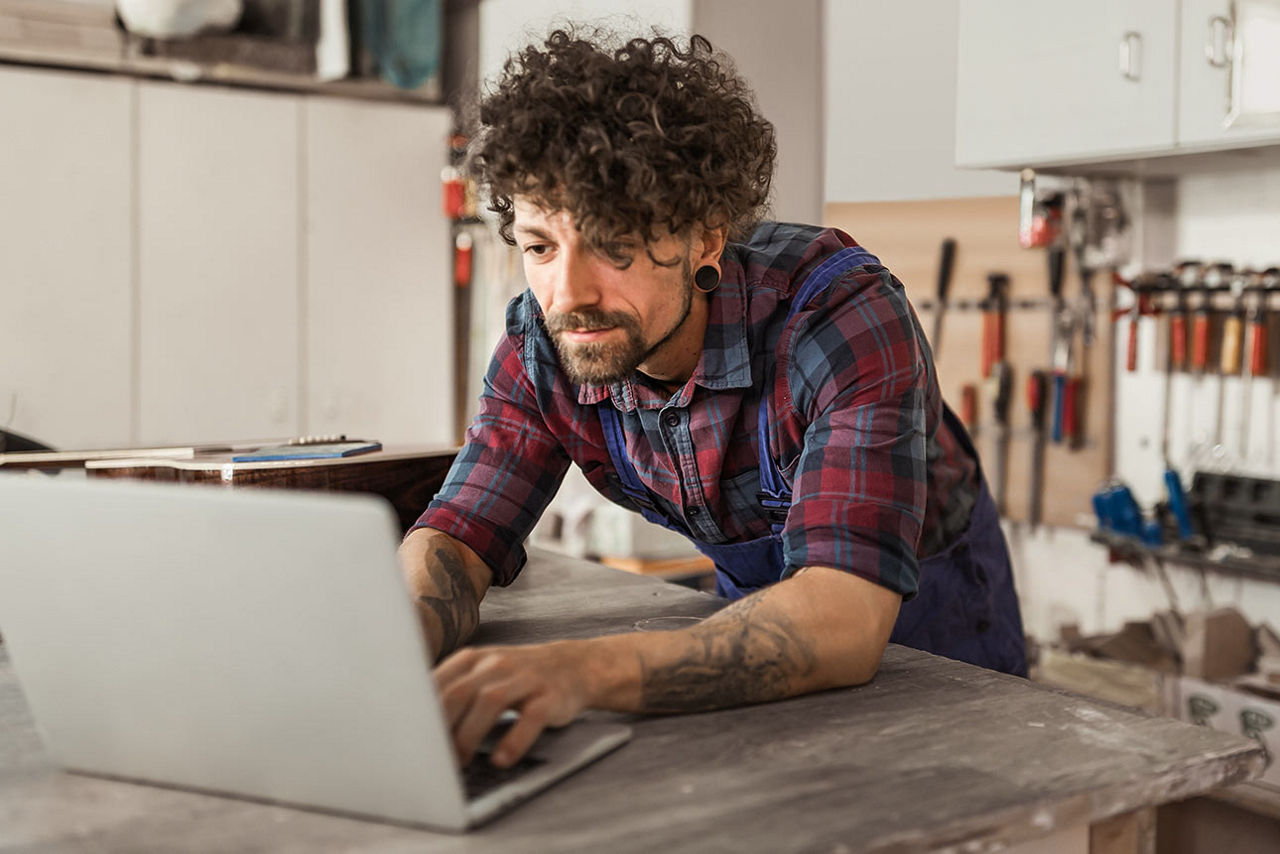 Ein junger Mann arbeitet auf seiner Werkbank an seinem Notebook