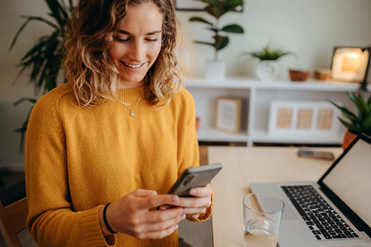 Eine junge Frau schaut lächelnd auf ihr Handy im Büro