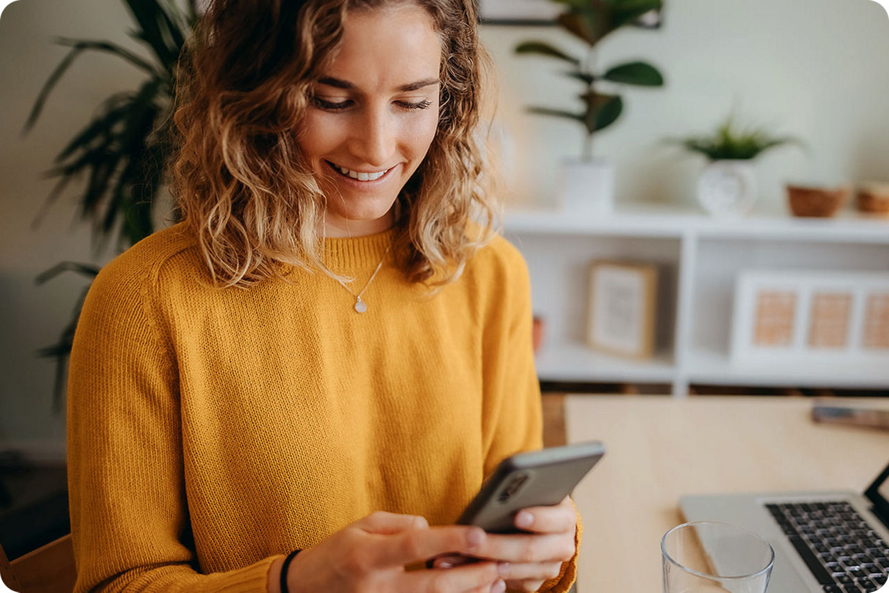 Ein Frau mit gelbem Pullover schaut auf ihr Smartphone