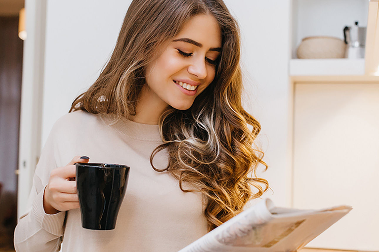 Frau liest ein Magazin mit einer Tasse in der Hand