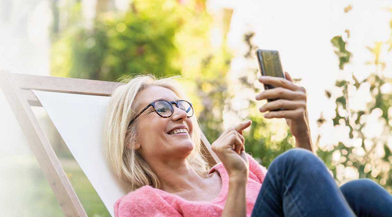 Festgeld - Frau mit Brille liegt und hat das Handy in der Hand