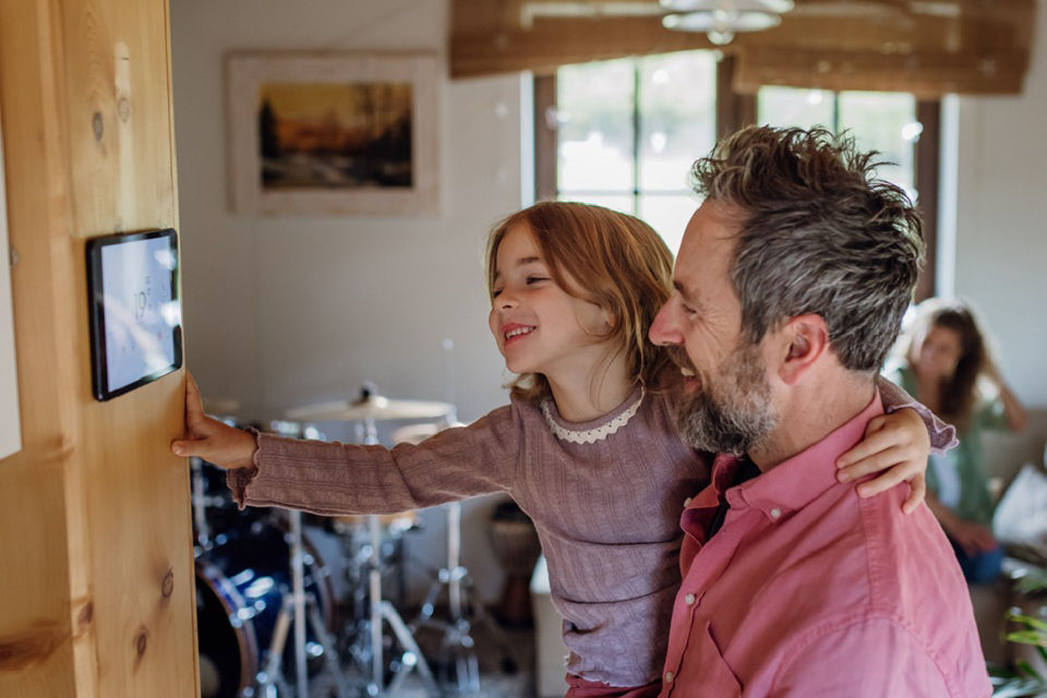 Vater mit Kind auf dem Arm schauen sich das Heizung Kontrollpanel im Haus an