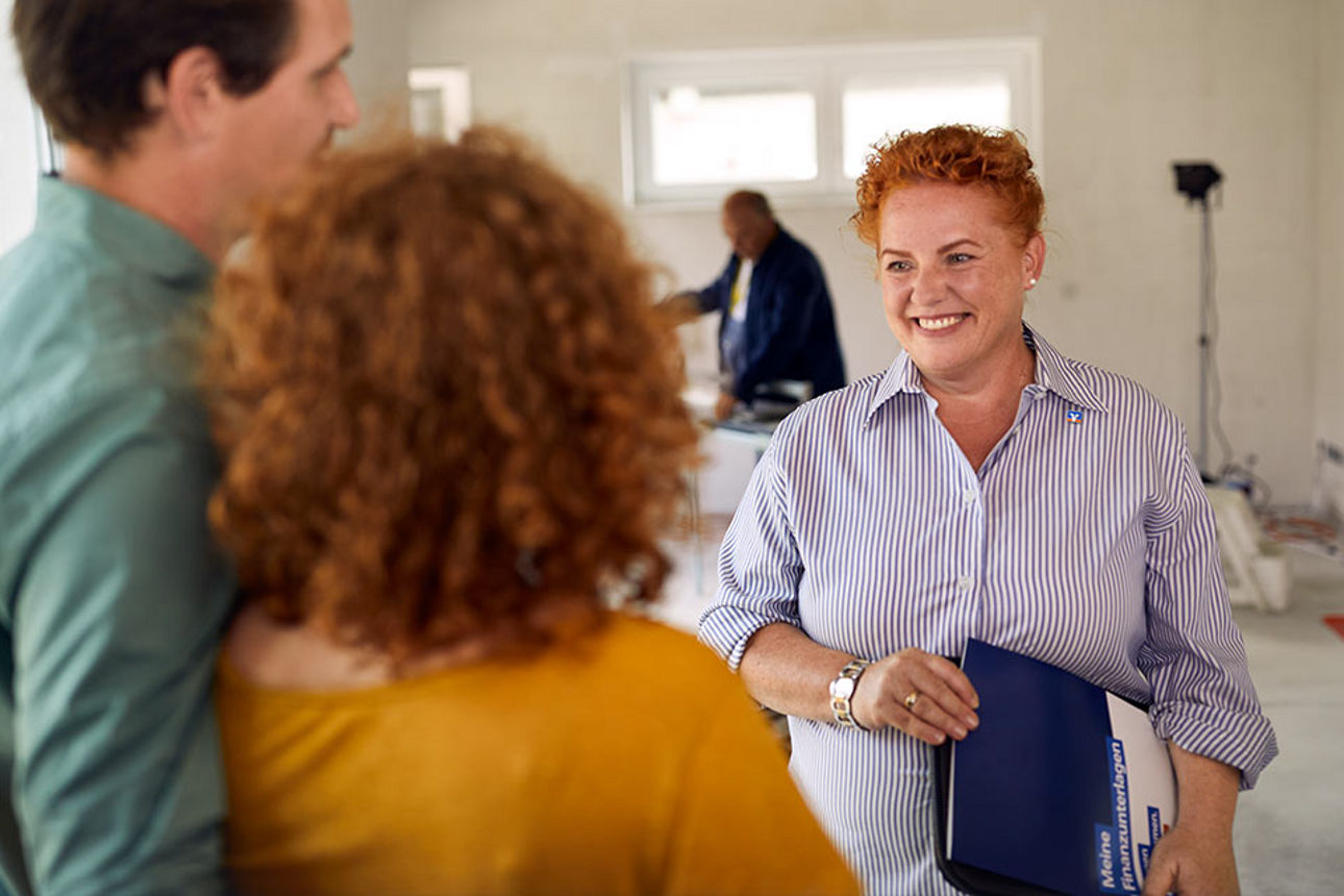 Ein junges Paar unterhält sich mit einer Beraterin in einem Rohbau
