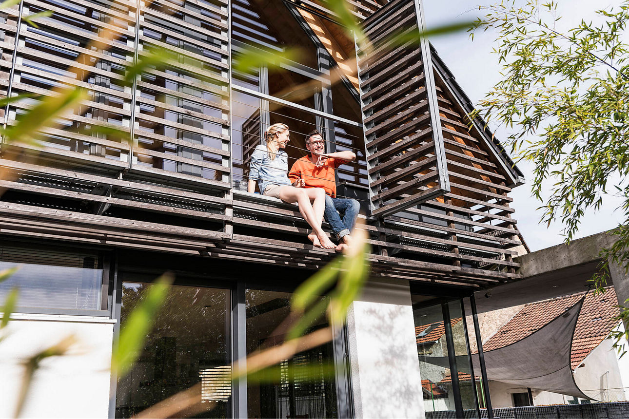 Zwei Personen sitzen am Balkon eines Wohnhauses