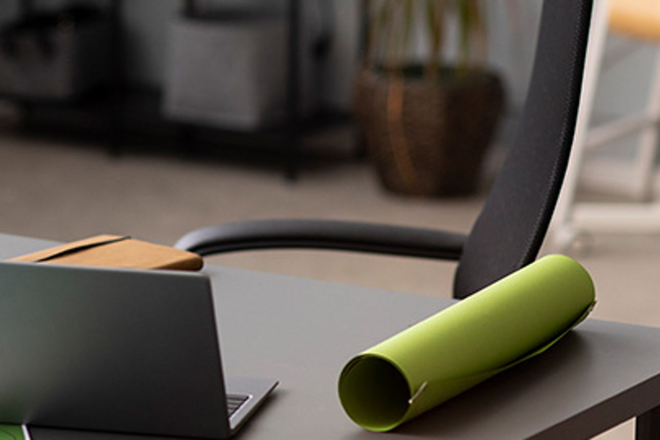 Ein Laptop auf einem Schreibtisch mit einem Gewächshausmodell und Windrädern im Hintergrund