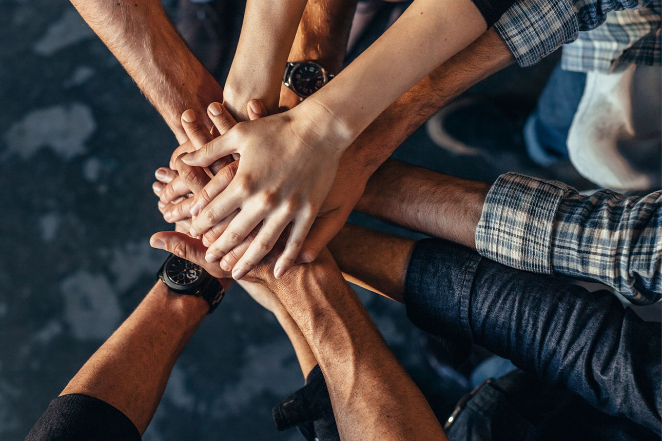 Viele Hände werden in die Mitte gehalten und symbolisieren Zusammenhalt