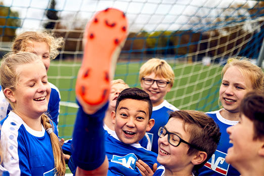 Kinder in Fußballtrikots lassen ein weiteres Kind hochleben