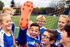 Kinder in Fußballtrikots lassen ein weiteres Kind hochleben