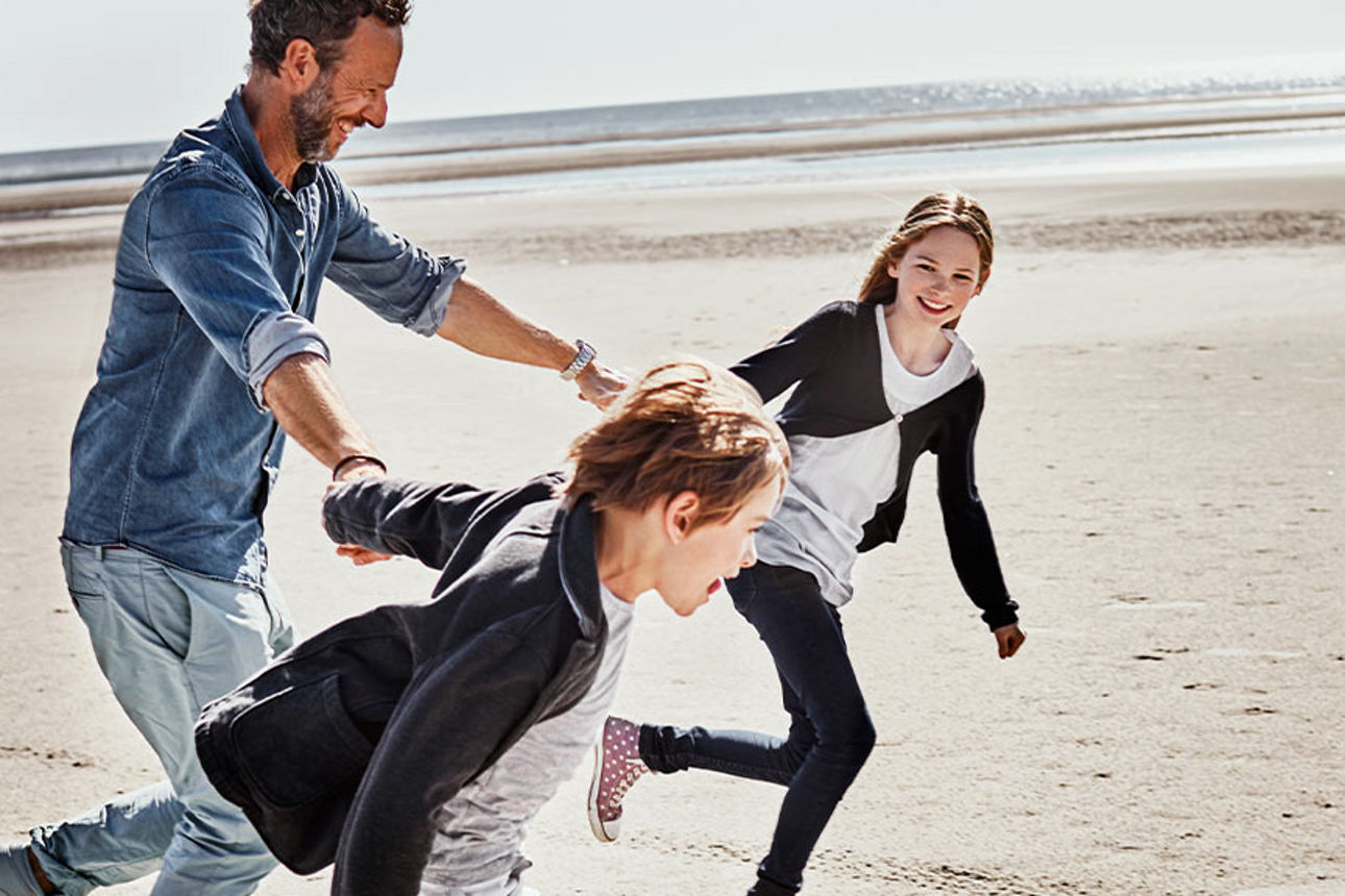 Ein Vater und seine zwei Kinder rennen Hand in Hand am Strand