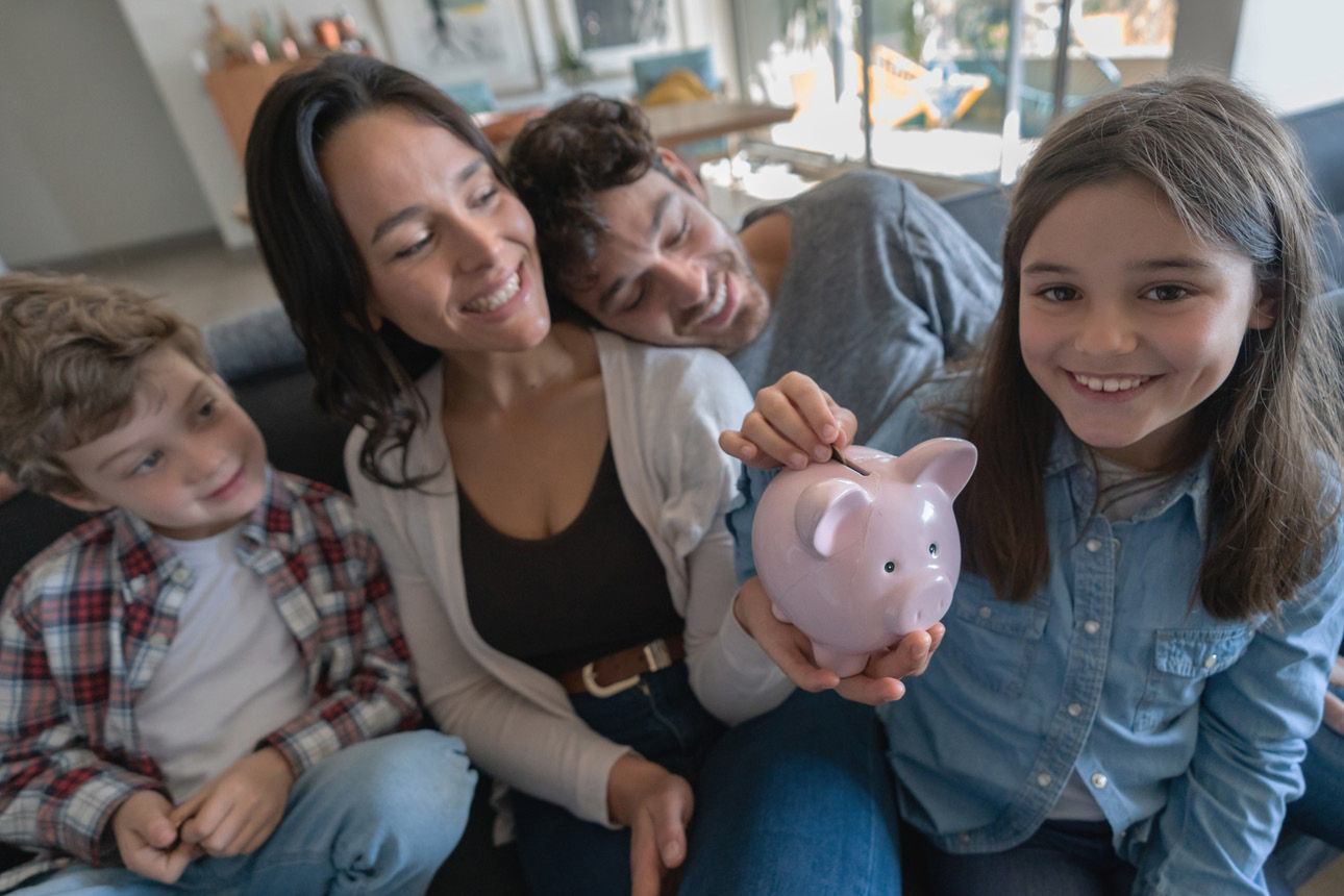 Eine Familie auf dem Sofa wirft ein Geldstück in ein Sparschwein