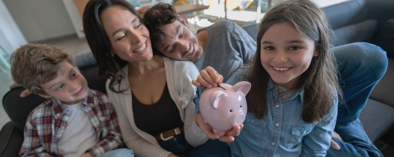 Eine Familie auf dem Sofa wirft ein Geldstück in ein Sparschwein