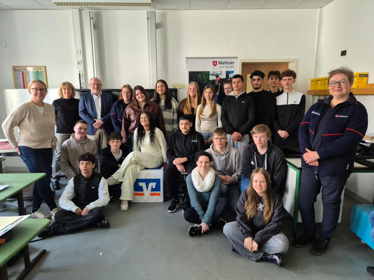 Auf dem Bild ist eine größere Gruppe von Jugendlichen und Erwachsenen in einem Klassenraum zu sehen.